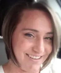 A woman with short brown hair smiling brightly while sitting inside a car.